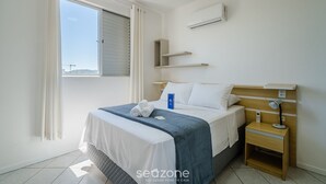 A bedroom with a bed, bedside table, air conditioning unit, and a window with curtains. - Apartments 230m From the Beach in Ingleses - ZIO (Florianópolis)
