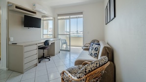 A modern living room with a flat-screen TV, a desk, a chair, a sofa with patterned cushions, and a ceiling fan. - Apartments 230m From the Beach in Ingleses - ZIO (Florianópolis)
