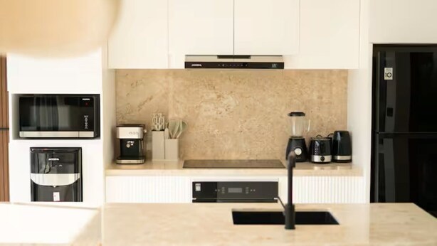 Una cocina moderna con armarios blancos, microondas integrado, cafetera y licuadora en la encimera.