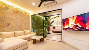 Una sala de estar moderna con una pared de piedra, un sofá color beige, una mesa de centro y un televisor mostrando una chimenea.