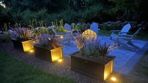 Ein Gartenbereich mit Sitzgelegenheiten und beleuchteten Pflanzgefäßen.