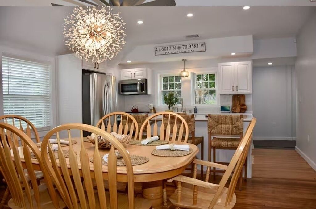 A modern kitchen with white cabinets, a stainless steel refrigerator, and a dining area with wooden chairs and a round table.