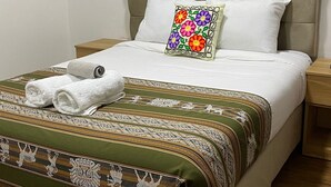Un lit bien fait, avec une couvre-lit à motifs, des oreillers blancs et un coussin aux couleurs vives, orné de motifs floraux.