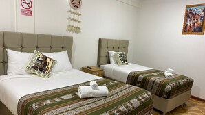 Une chambre d’hôtel avec deux lits, chacun agrémenté de draps et d’oreillers à motifs, d’une décoration suspendue, d’un tableau au mur et d’un panneau indiquant qu’il est interdit de fumer.