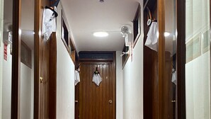 Un couloir avec des portes en bois et un sol carrelé, qui mène à une porte dotée d’une petite fenêtre.