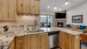 A kitchen with wooden cabinets, a dishwasher, a granite countertop, and a stone fireplace.