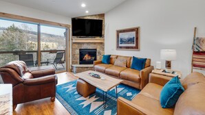 A spacious living room with a stone fireplace, leather sofas, a coffee table, and a large window offering a view of the outdoors.