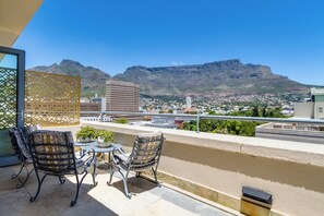 A balcony with two chairs and a small table, overlooking a cityscape with mountains in the background. - Tranquil 3-bedroom apartment with AC in Cape Town (Cape Town)