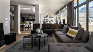 Una sala de estar moderna con un sofá, una mesa de centro y un televisor. Se observa un comedor al fondo con una mesa y sillas.