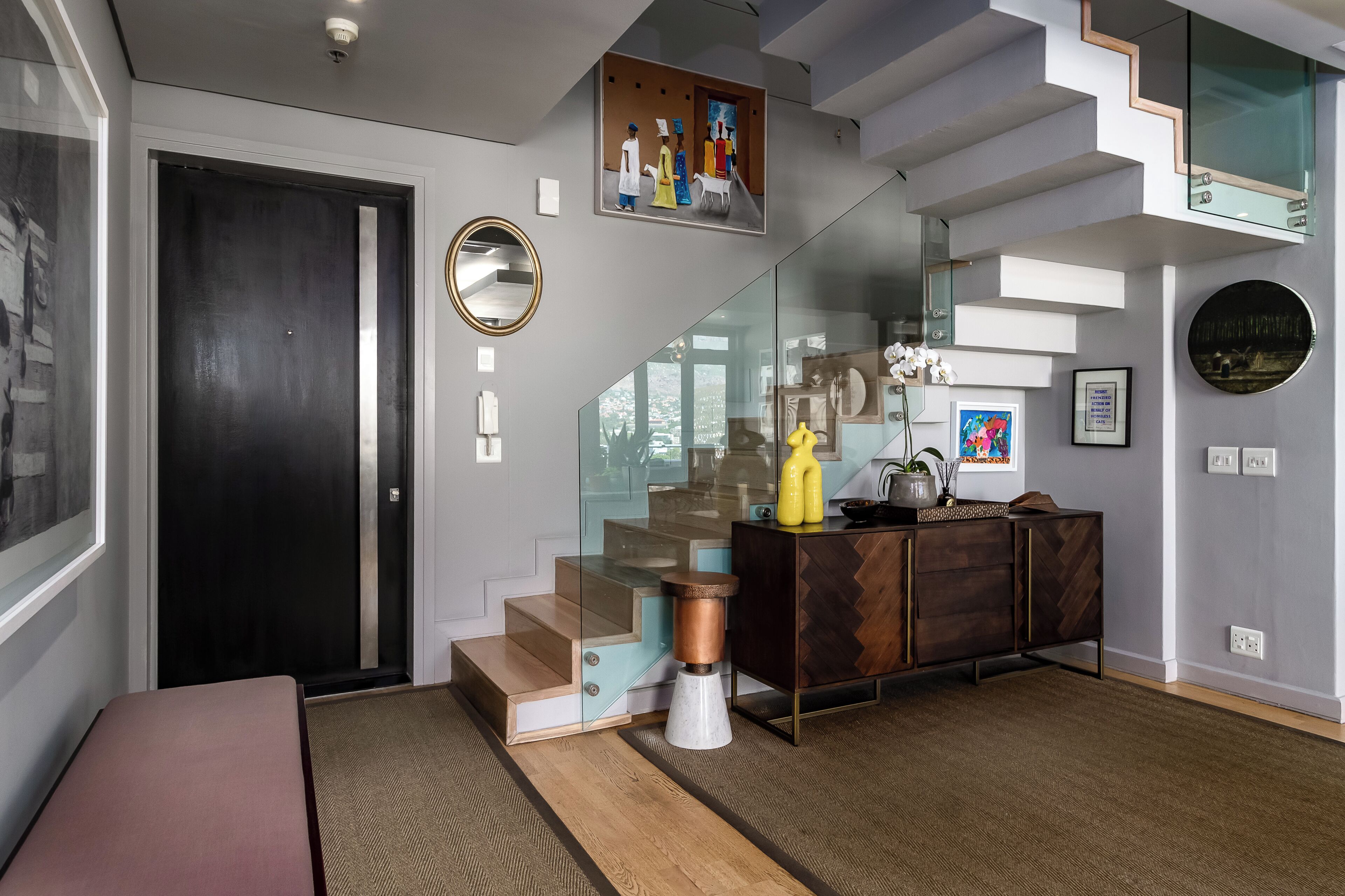 A modern interior with a staircase, a bench, a cabinet, and a wall-mounted picture.