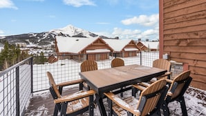 Una terraza de madera con una mesa y sillas, con vistas a una montaña nevada y un pueblo.