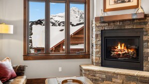 Una sala de estar acogedora con chimenea, un ventanal con vistas a una montaña nevada y un banco de madera.