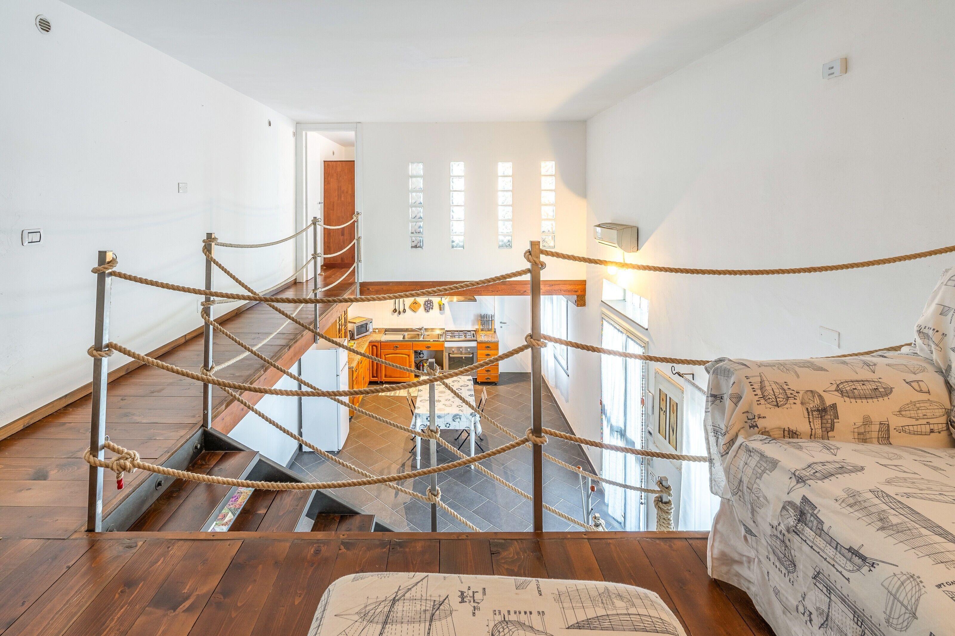 Ein Zimmer mit hohen Decken, einer Treppe, einer Küchenzeile und einem Sofa mit maritimem Bettbezug.