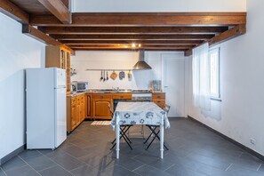 A kitchen with wooden cabinets, a white refrigerator, a dining table with a tablecloth, and a window with curtains.