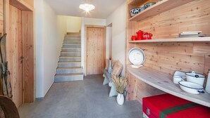 Un intérieur en bois avec un escalier, une valise rouge et des étagères remplies d’assiettes et d’un pot rouge.