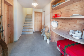 Un intérieur en bois avec un escalier, une valise rouge et des étagères remplies d’assiettes et d’un pot rouge.
