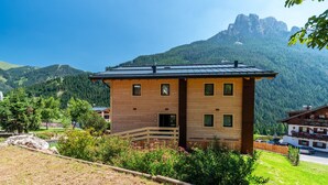 Un bâtiment en bois à deux étages, doté d’un balcon, entouré de verdure et bordé de montagnes.