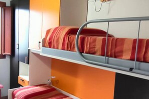 Un lit superposé avec une literie orange, un mur blanc et une armoire en bois.