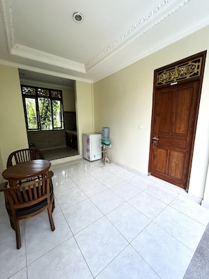 A room with a wooden door, a water dispenser, a refrigerator, and a dining table with chairs. - balimas guest house (Ubud)