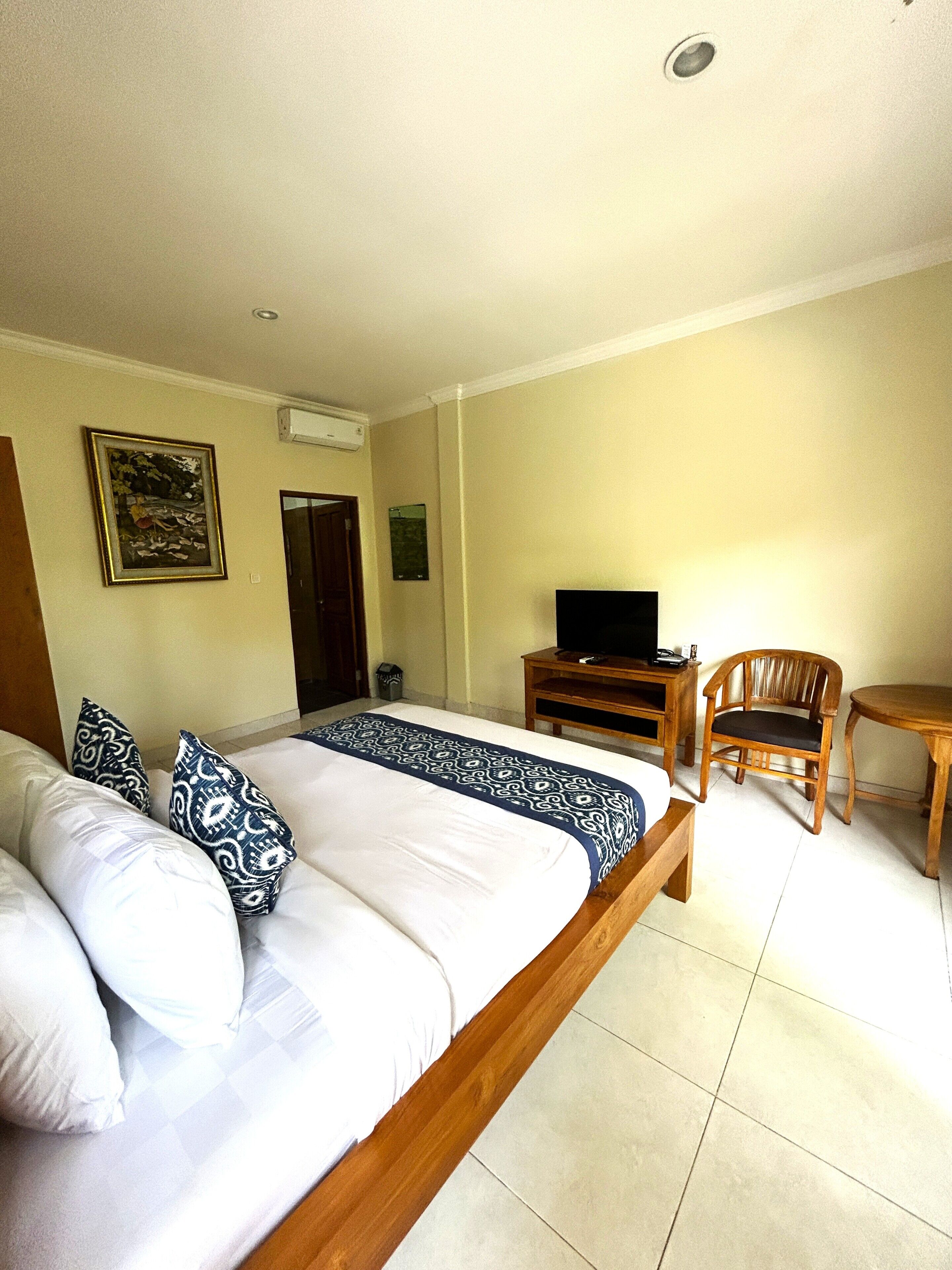 A hotel room with a bed, a television, a wooden chair, and a small table.