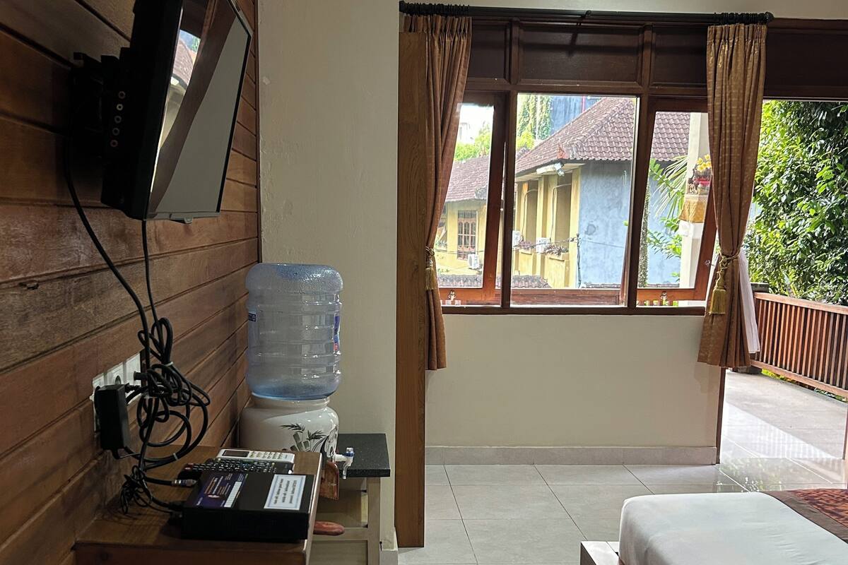 Une chambre d’hôtel comprenant un lit, un bureau avec un ordinateur, un distributeur d’eau, un téléviseur fixé au mur et une fenêtre avec des rideaux.