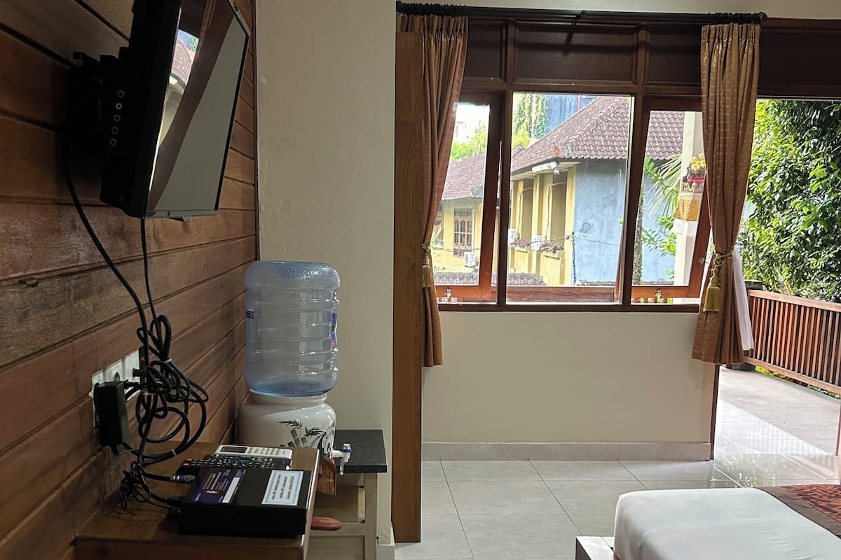 A hotel room with a bed, a desk with a computer, a water dispenser, a TV mounted on the wall, and a window with curtains.