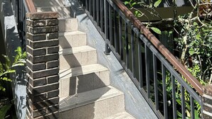 Una escalera con un pilar de ladrillo, barandilla de madera y vista a un edificio con balcón.