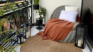 A balcony with a bed, macramé wall hangings, potted plants, and a woven rug. - Simba Heights Kyanja (Kampala)