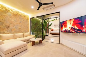 Ein modernes Wohnzimmer mit einer Wand aus Stein, einem großen Flachbildfernseher, einem Deckenventilator und einer Glastür, die in ein Schlafzimmer führt.