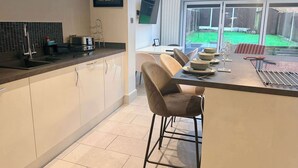 A modern kitchen with a central island, a dining area with chairs, and a view of the backyard through large windows.