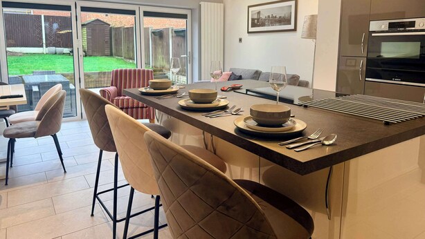 A modern kitchen with a large island, a dining area with chairs, and a view of the backyard through glass doors.