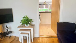 A living room with a TV, a small table with a plant, a wooden bench, and a dark-colored sofa.