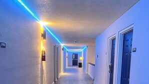 A hallway with a wooden floor, white walls, and blue LED lighting along the ceiling. - Charming King Studio (Interior) (Lafayette)