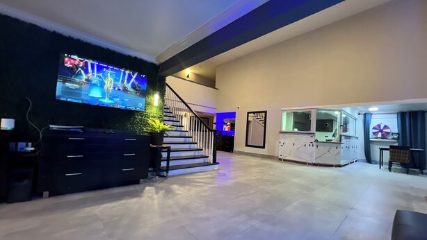 A spacious living area with a large flat-screen TV mounted on a dark wall, a staircase with blue lighting, and a kitchen area with a marble countertop. - Charming King Studio (Interior) (Lafayette)