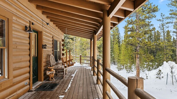 Una baita di legno con un portico coperto, un cartello di benvenuto e una sedia.