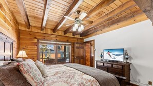 Una camera da letto con soffitto in legno, un letto con biancheria a motivi, una televisione su un comò in legno e una finestra con vista sull'esterno.