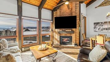 A cozy living room with a fireplace, large windows, and a view of a snowy landscape.