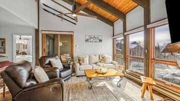 A spacious living room with a high ceiling, large windows, and a fireplace.