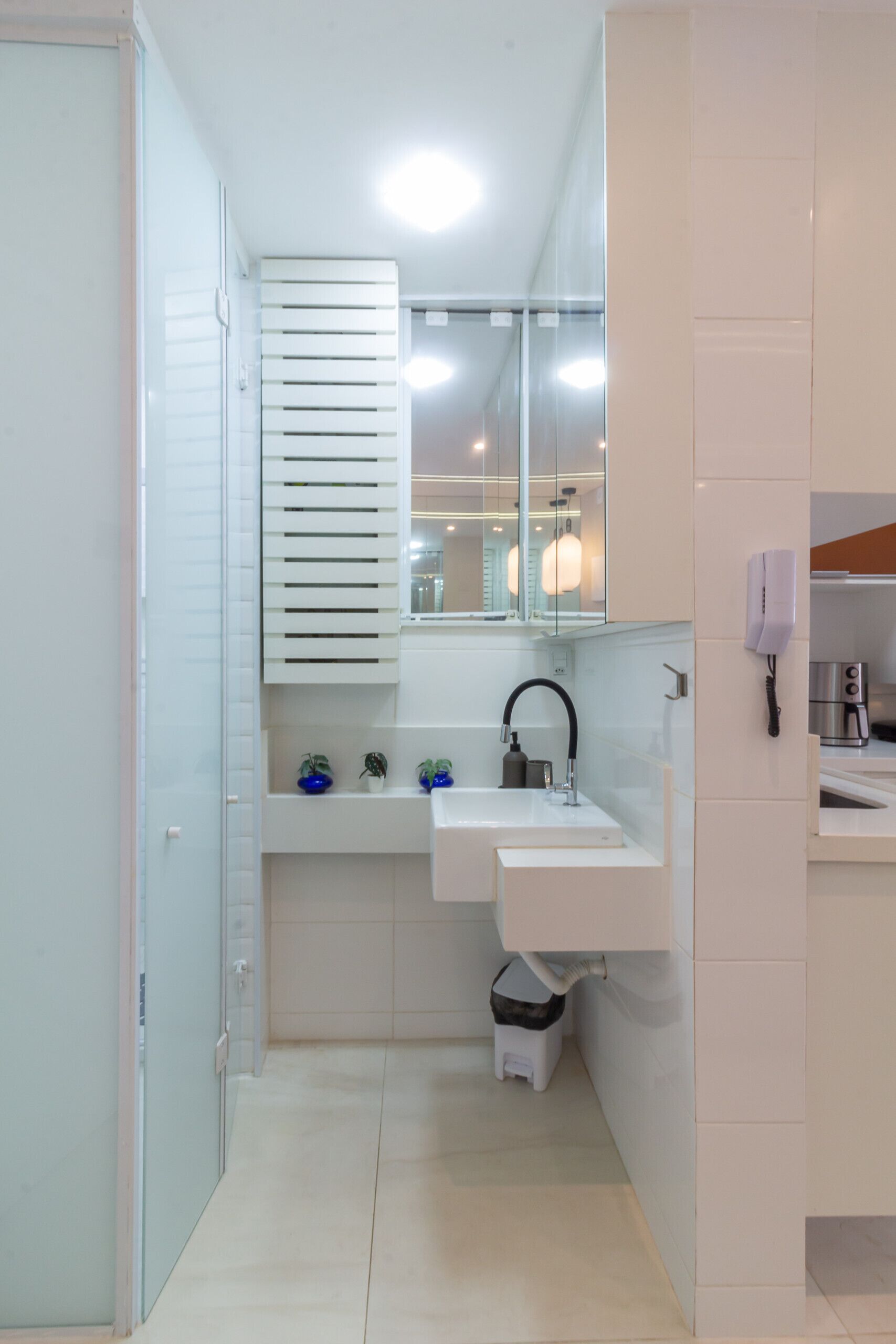 A modern bathroom with a white sink, mirror, and a small trash bin.