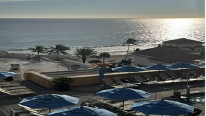 Ein Hotel am Strand mit Sonnenschirmen, Liegestühlen und Blick auf den Ozean.