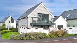 Une maison moderne à deux étages, dotée d’un balcon, d’une clôture en bois peinte en blanc et d’une pelouse bien entretenue.