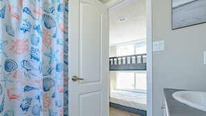A room with a bunk bed, a bathroom with a sink, and a curtain with a sea-themed pattern.
