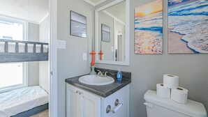 A bathroom with a sink, toilet, and a bunk bed in the adjacent room.