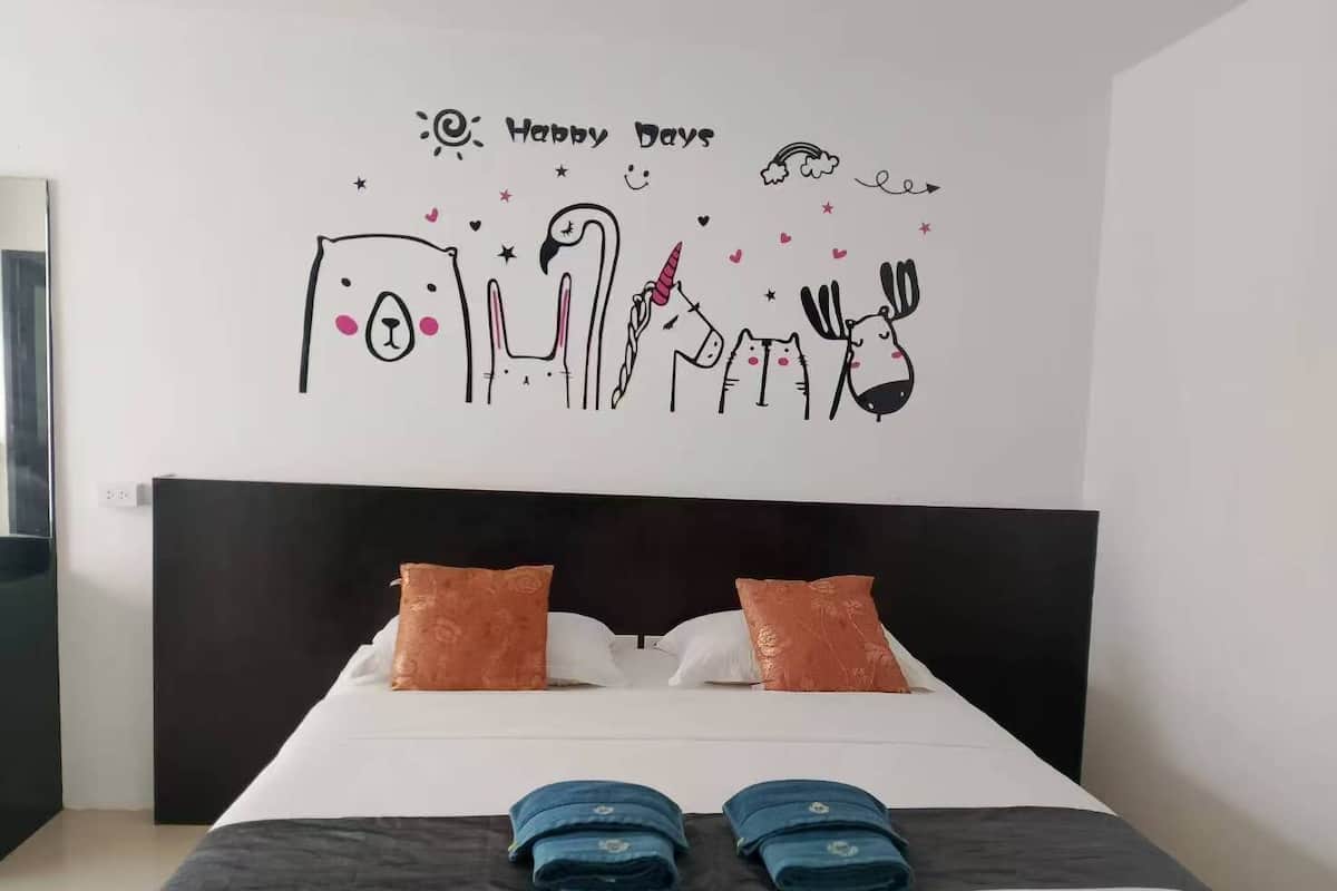 A neatly made bed with two pillows, a headboard, and a wall decal with a 'Happy Days' message.