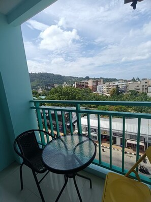 Un balcón con una mesa y sillas de vidrio, con vistas a un paisaje urbano de edificios y zonas verdes.