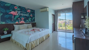 Quarto com cama, uma janela grande, varanda e um mural temático tropical.