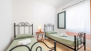 A room with two single beds, a small table, a wall-mounted mirror, and a window with curtains. - Relaxing Apartment Close to Santa Lucia Beach (Siniscola)