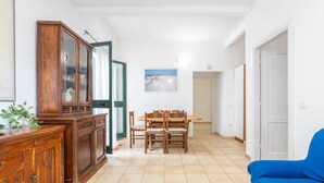 A dining area with a wooden table and chairs, a cabinet with glass doors, and a blue sofa. - Relaxing Apartment Close to Santa Lucia Beach (Siniscola)