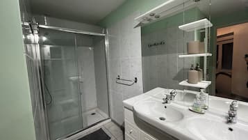 Un baño moderno con cabina de ducha de vidrio, un lavamanos blanco con espejo y un perchero para toallas.