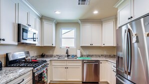 Una cocina moderna con armarios blancos, electrodomésticos de acero inoxidable, encimera de granito y una ventana con persianas.